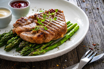 Barbecued pork neck and asparagus on wooden table