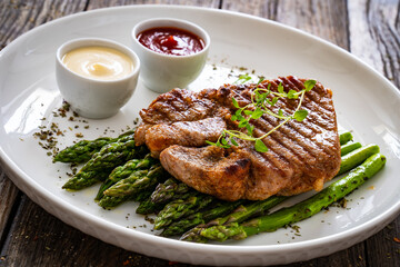 Barbecued pork neck and asparagus on wooden table