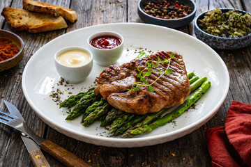 Barbecued pork neck and asparagus on wooden table