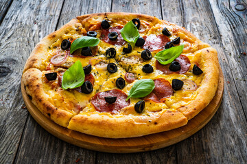 Circle pepperoni pizza with mozzarella cheese and black olives on wooden table
