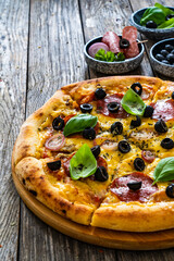 Circle pepperoni pizza with mozzarella cheese and black olives on wooden table
