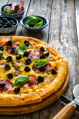 Circle pepperoni pizza with mozzarella cheese and black olives on wooden table
