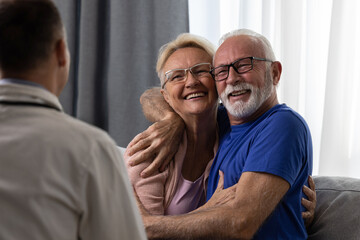 Happy senior couple hugging and feeling cheerful about good news at medical consultation. Smiling...