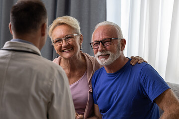 Healthy smiling senior couple feeling cheerful about good news at medical consultation. Happy eldelrly man and woman talking to a doctor at appointment. - 602219823