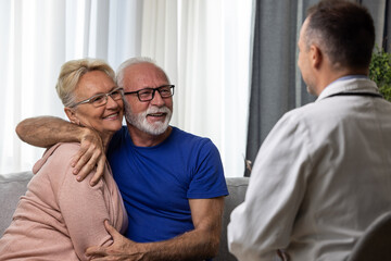 Happy senior couple hugging and feeling cheerful about good news at medical consultation. Smiling eldelrly man and woman talking to a doctor at appointment.
