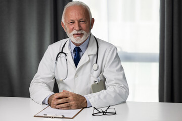 Portrait of senior male doctor, sitting by the table and looking at a camera. Medical director...