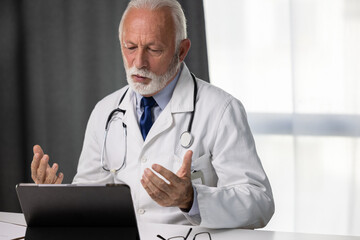 Senior male doctor consulting patient through online video call using tablet PC. Or medical...