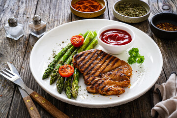 Barbecued meat and asparagus on wooden table