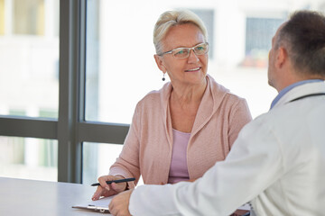 Senior woman filling insurance or other legal document at appointment with doctor. Elderly patient signing medical treatment contract, agreement form for medical care service, consultation, therapy