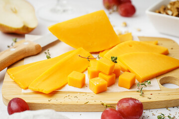 Wooden board with tasty cheddar cheese on light background