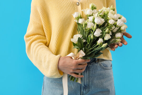 Young woman with bouquet of beautiful eustoma flowers on blue background