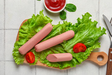 Board of tasty sausages with lettuce and tomatoes on white tile background