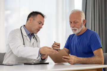 Senior man filling insurance or other legal document at appointment with doctor. Elderly patient...