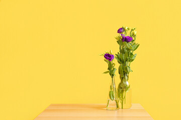 Vase with eustoma flowers on table near yellow wall