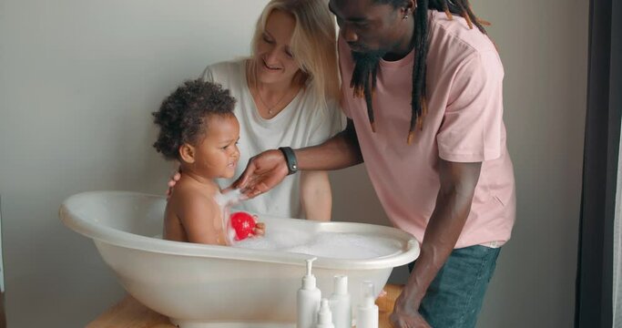 happy African father and Caucasian mother giving adorable toddler girl bath slow motion Daily routine water procedures lifestyle Free Spare time parenthood fatherhood motherhood