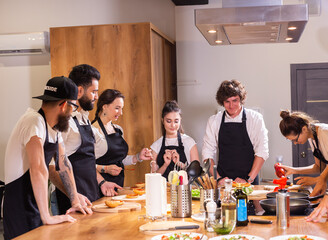 Cooking course - senior male chef in cook uniform teaches young people cooking class students to...