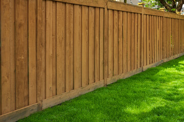 Nice new wooden fence around house. Wooden brown fence with green grass lawn. Street photo