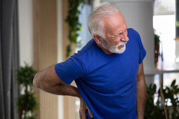 Elderly man holding hand on his lower back, suffering from osteoarthritis pain at home