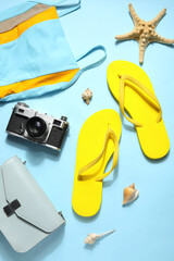 Flip flops with swimsuit, camera and bag on pale blue background