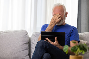 Senior man using digital tablet computer at home and having eyestrain or suffering from astigmatism and bad vision. Eyesight problems concept. - 602222498