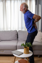 Elderly man holding hand on his lower back, suffering from osteoarthritis pain at home
