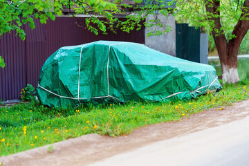 The car is covered with a homemade green cape near a private house