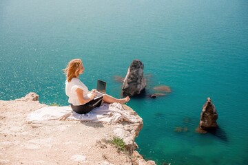 Freelance woman working on a laptop by the sea, typing away on the keyboard while enjoying the beautiful view, highlighting the idea of remote work.