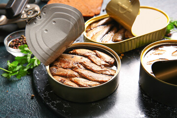 Board of canned smoked sprats on dark background