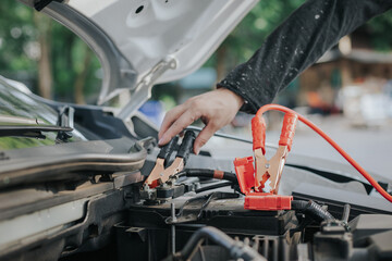 Close-up of auto mechanic charging car battery with electric rail jumper cables