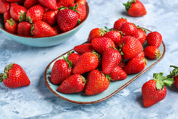 Bowl and plate with fresh strawberries on blue background
