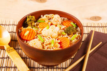 Traditional Asian instant noodles accompanied by vegetables placed on wooden backdrop.