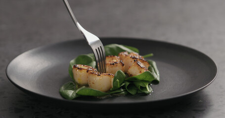 eating roasted scallops with spinach in black plate
