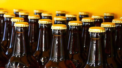 Many dark glass bottles of beer with yellow metallic caps against yellow background