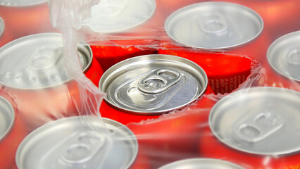 Close-up of many red cans of beer in plastic packaging torn from the top