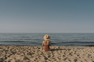 Pretty woman sitting on beach sand and watching at sea and sky. Minimal summer vacation concept....