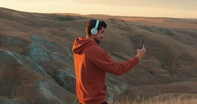 Happy man hold smartphone, making video call, taking picure, photo in mountains evening. Smiling muscular man enjoying podcast audiobook on outdoor activity Social media device concept Guy uses gadget