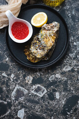 Cast-iron tray with unopened oyster and red caviar, above view on a dark-brown granite background, vertical shot, copy space