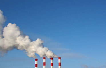 Industrial chimneys with white smoke against blue sky. Tall pipes with steam on a winter day.