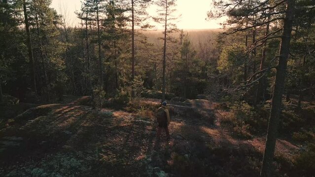 A naturephotographer walking on the forest cliff towards sunset. Taking pictures of the forest.