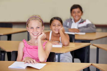 Portrait, kids and smile of student in classroom with book, ready to learn and study in class. Group of students, education and girl learning in primary school for knowledge, development or studying.