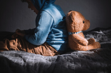 A sad little boy sits back to back with a teddy bear. Autistic Spectrum Disorder. the child does not want to make contact with others