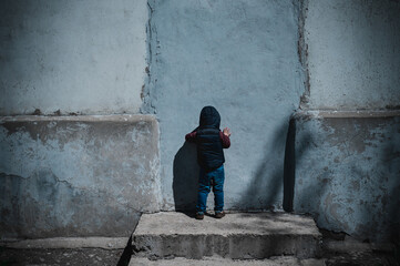 A sad little boy looks at the wall with his own shadow. Autistic spectrum disorder symptom. Lonely child sadness despair and depression. Back view