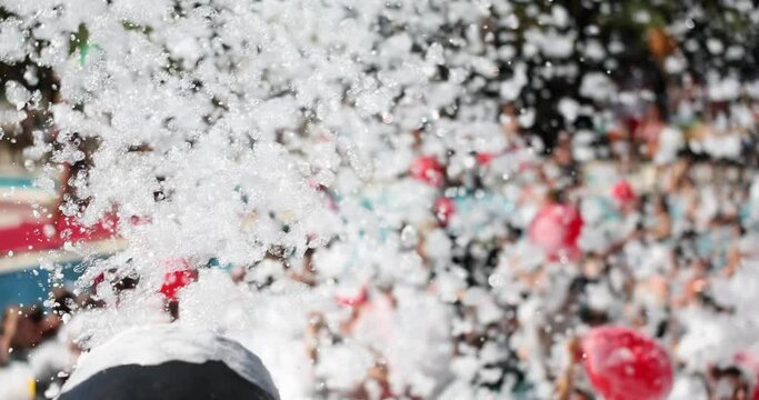 Automatic foam machine shoots with froth at poolside foam party in daytime. Mechanical equipment for fun holidays. Wet fluffy substation producing slow motion
