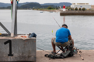 Un jubilado pesca en un puerto de mar sentado con su caña. © time and light