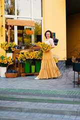 Naklejka premium Elegant smiling woman with a bouquet of sunflowers flowers near a cafe - a flower shop.