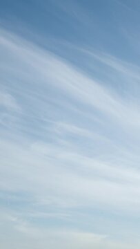With a serene and crystal-clear sky, the light-as-a-feather cirrus clouds lazily traverse the heavens. Video timelapse. Vertical video.