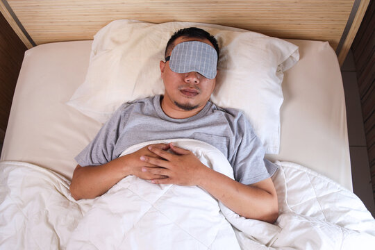 Top view of young asian man in eye mask sleeping in bed at home