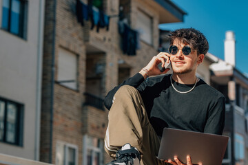 young man with mobile phone and laptop outdoors
