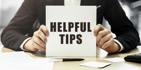 Businessman holding a white card with text Helpful tips on office background