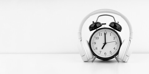 Black alarm clock with headphones on white wall background